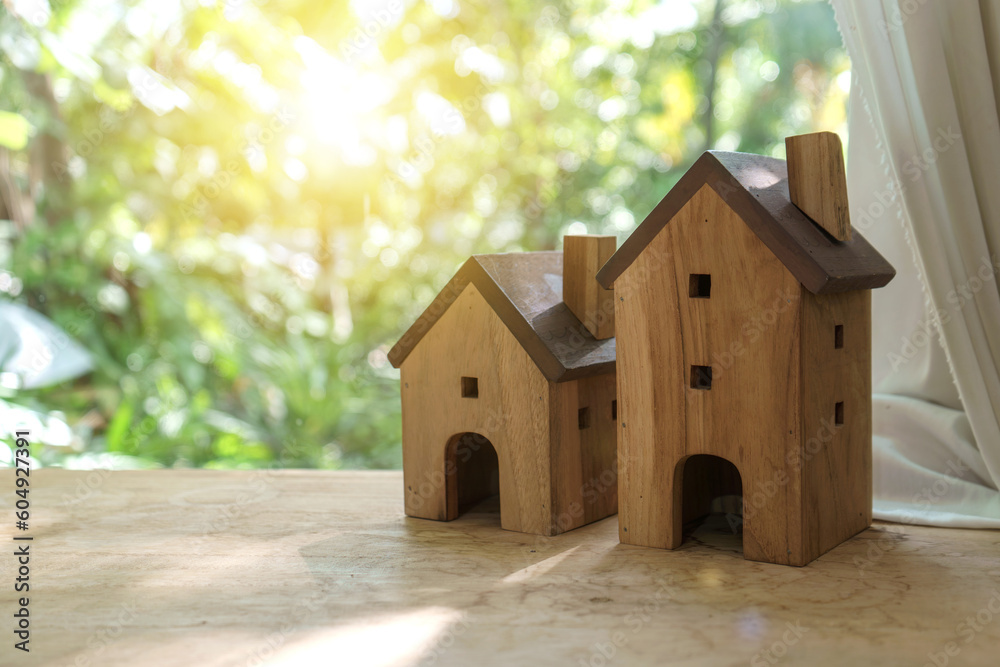 A simple classic wooden house model is placed on the table by the window. With a natural garden background with morning sunlight. A simple classic wooden house model is placed on the table by the window. With a natural garden background with morning sunlight.