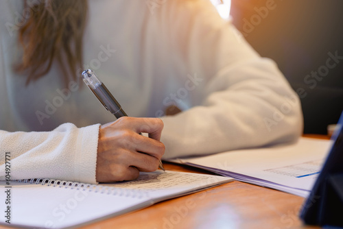 Close-up of university students writing on notebook with tablet on the table