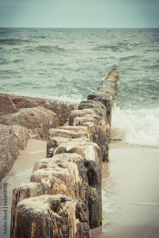 Scenic view of wooden breakwaters and sea waves at beach. Stormy day at sea