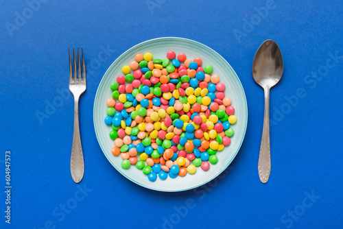 cutlery on table and sweet plate of candy. Health and obesity concept, top view on colored background