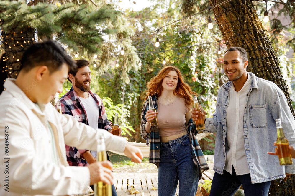 A young, cheerful, multiracial company is relaxing outside the city. People of different genders are dancing near the tourist trailer, drinking drinks, having fun.