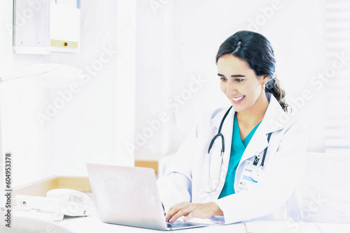 Beautiful and professional female doctor using laptop computer, working at her desk in the doctor's office.