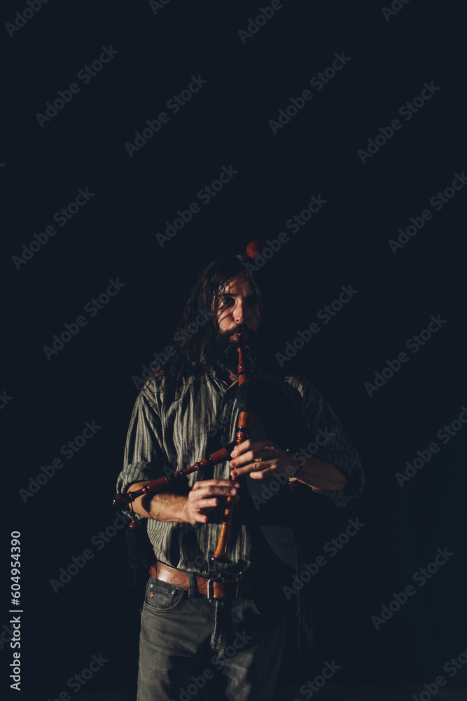 Bagpipe player playing his instrument in an auditorium with stage lights and a black background. Bagpipe player playing his instrument in an auditorium with stage lights and a black background.