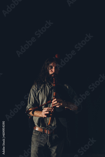 Bagpipe player playing his instrument in an auditorium with stage lights and a black background.