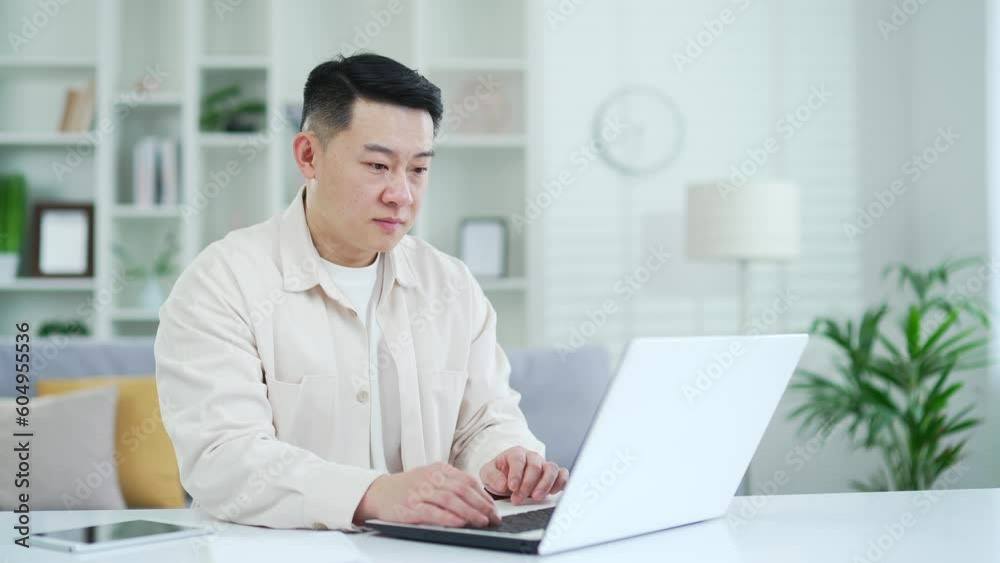 Disappointed asian man read bad news on laptop while sitting at desk at workplace in home office. Sad male freelancer upset by unpleasant notification, shocked by information seen on the Internet Disappointed asian man read bad news on laptop while sitting at desk at workplace in home office. Sad male freelancer upset by unpleasant notification, shocked by information seen on the Internet