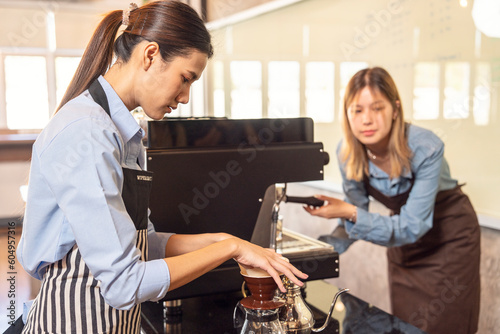 Barita girl grinding coffee and roasting coffee with a coffee machine trains new employee training. Two girls take notes at the counter in a coffee shop photo