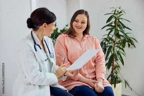 A smiling overweight woman sitting with a female nutritionist during the examination.