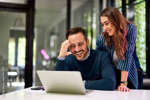 A male and female colleague looking for something funny on a laptop at the office.