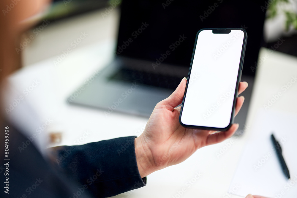 An adult woman holding a mobile phone with a blank white screen, indoors.