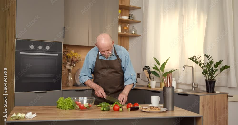 Senior man in apron cooking some healthy salad in the kitchen Senior man in apron cooking some healthy salad in the kitchen