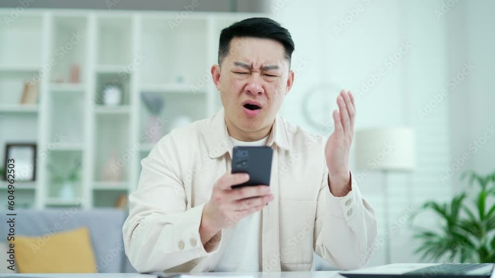 Disappointed asian man read bad news on smartphone while sitting in home office. Sad male freelancer upset by unpleasant notification, shocked by information seen on the Internet, depressed by message Disappointed asian man read bad news on smartphone while sitting in home office. Sad male freelancer upset by unpleasant notification, shocked by information seen on the Internet, depressed by message