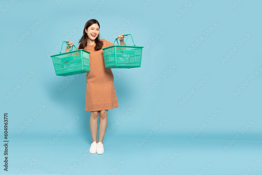Asian woman smiling and holding grocery basket isolated on light blue background, Shopping and Supermarket concept Asian woman smiling and holding grocery basket isolated on light blue background, Shopping and Supermarket concept