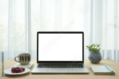 Fototapeta Naklejka Na Ścianę i Meble -  white screen laptop and notebooks and coffee cup and flowers on wooden table in front of window
