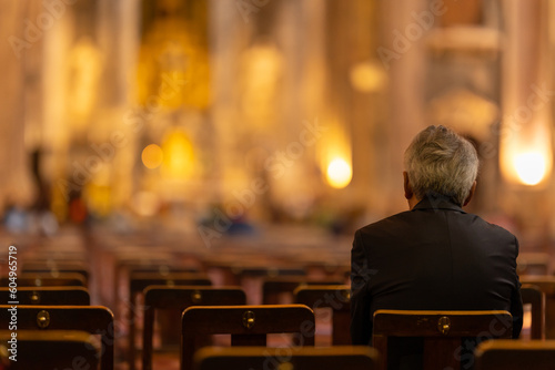 An elderly man sits on a chair in a church