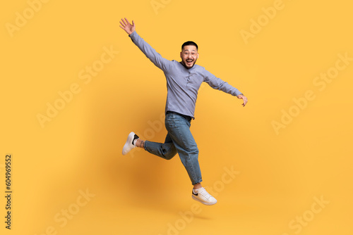 Happy Excited Asian Man Jumping In Air On Yellow Background © Prostock-studio