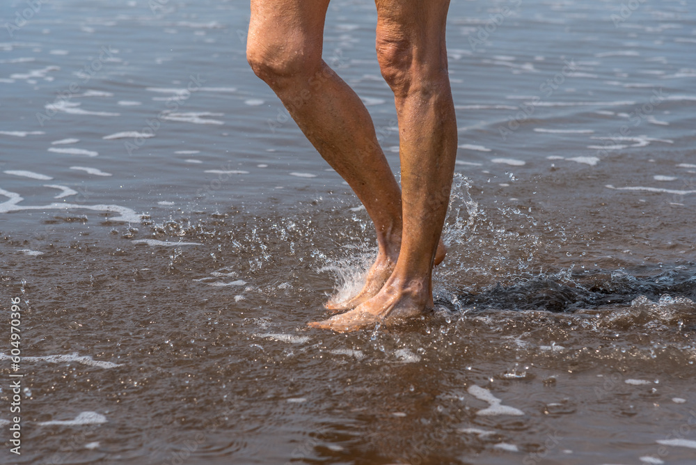 Barefoot person walking along the seashore on the beach.