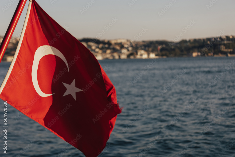 A red flag with a white star on Turkey flag and Istanbul view. Boat view of the national flag of Turkey and the coastline of Istanbul during the Bosphorus cruise.