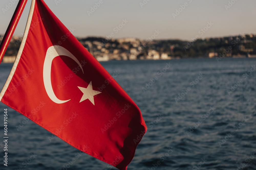 A flag with a city in the backgroundTurkish Flag, Bosphorus and cityscape of Istanbul on the background. Turkish national days concept.