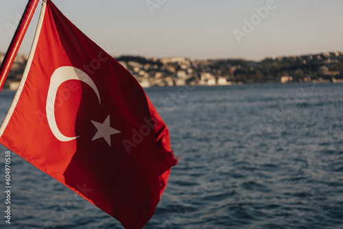Obraz na płótnie A red flag with a white star on Turkey flag and Istanbul view. Boat view of the national flag of Turkey and the coastline of Istanbul during the Bosphorus cruise.
w salonie