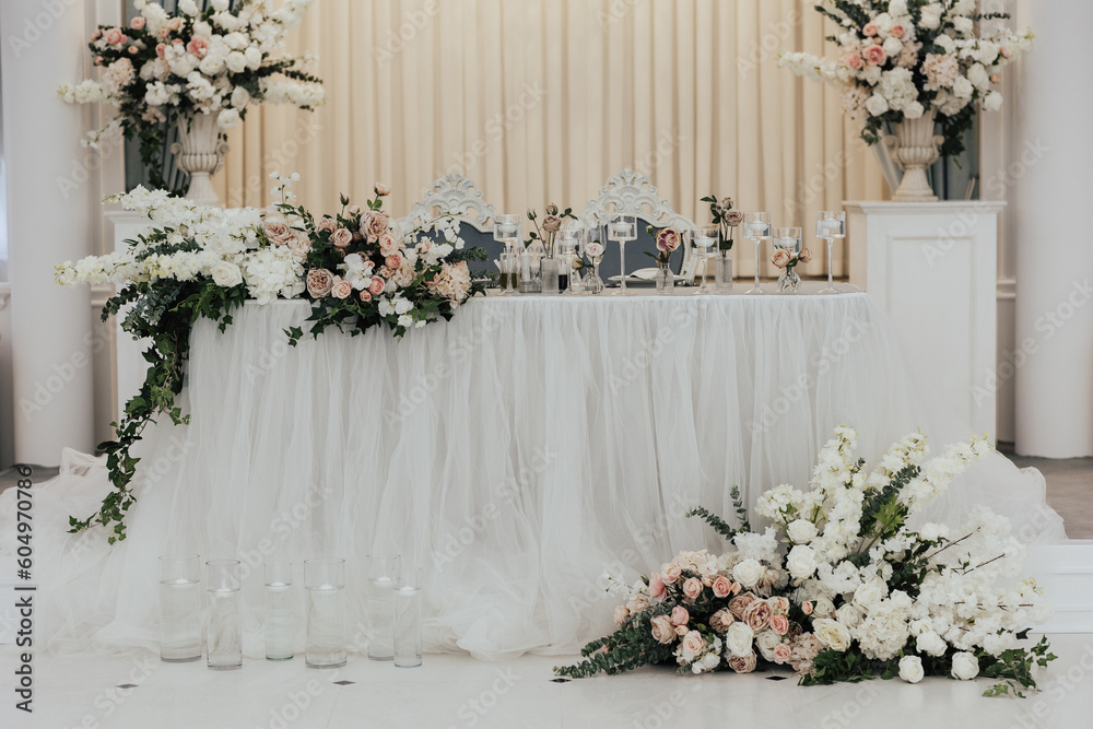 Wedding presidium. Banquet table for newlyweds with flowers, greenery and candles. Lush floral arrangements in vases. Classic wedding.