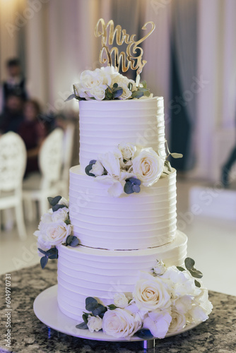 Beautiful white three-tiered wedding cake decorated with natural flowers.Wedding cake with floral decoration.	
