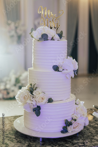 Beautiful white three-tiered wedding cake decorated with natural flowers.Wedding cake with floral decoration.	
