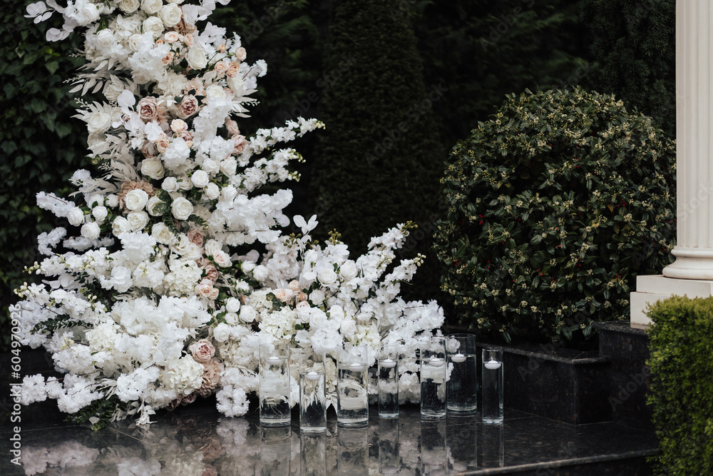 A detail of wedding arch decorated with a composition of white flowers for an outdoor wedding ceremony. Classic wedding decor with candles.