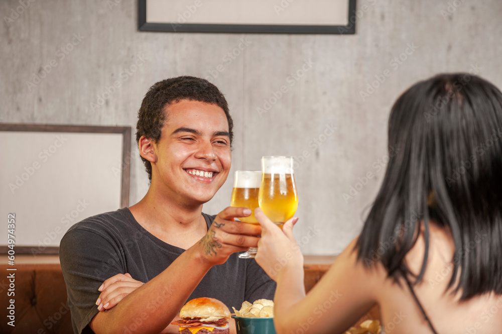 Happy couple toasting with beer at pub restaurant fast food table with burger. Happy couple toasting with beer at pub restaurant fast food table with burger.
