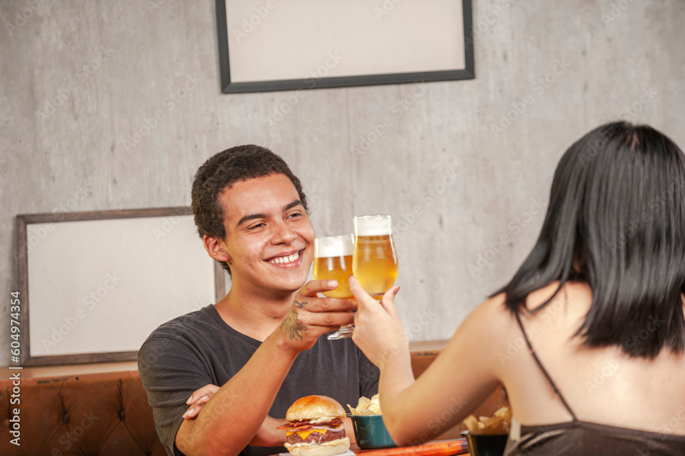 Happy couple toasting with beer at pub restaurant fast food table with burger. Happy couple toasting with beer at pub restaurant fast food table with burger.