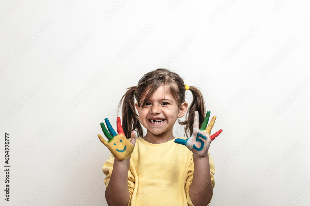 Happy toothless little girl with the five number painted on the hand laughing and having fun - Little girl painting her hands with smiley faces and numbers - The number five and childhood concept