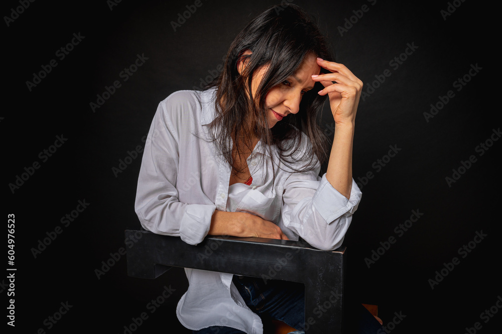 business portrait of a young girl around 40 years old, cute, emotional thoughtful, sitting on a high chair on a dark background, studio shot with copy space business portrait of a young girl around 40 years old, cute, emotional thoughtful, sitting on a high chair on a dark background, studio shot with copy space