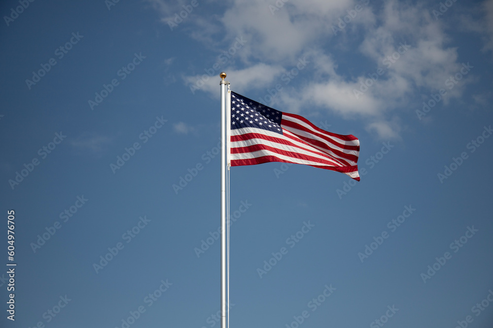 American flag displayed on flagpole with blue sky background on a breezy day. American flag displayed on flagpole with blue sky background on a breezy day.