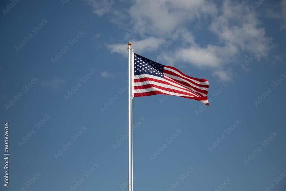 American flag displayed on flagpole with blue sky background on a breezy day.