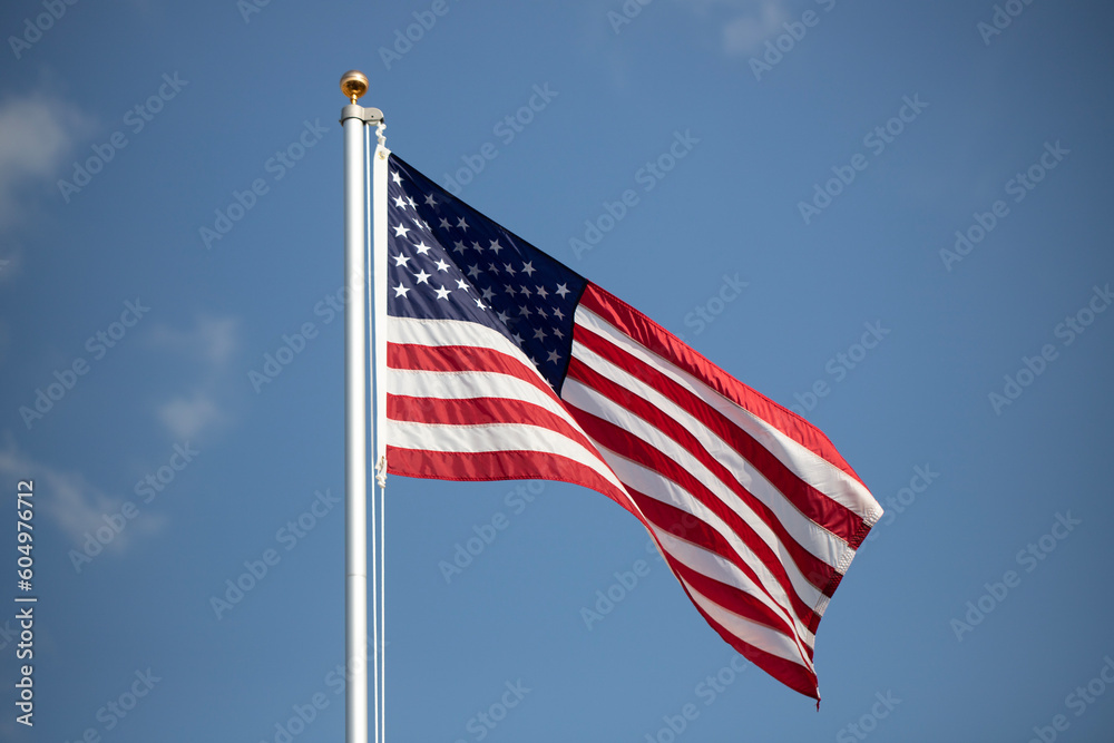 American flag displayed on flagpole with blue sky background on a breezy day.