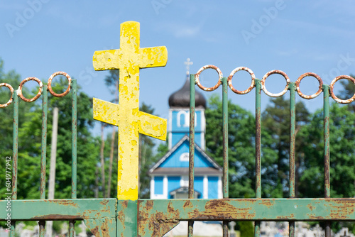 Orthodox cross isolated. Cementry in the background. Old, rusty metal faith symbol. East of Poland. Rusty metal gate. Orthodox wooden church. Countryside small church made of blue wood.