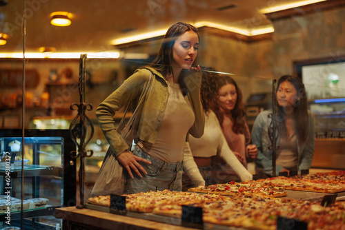 Young woman looking at pizza while standing in bakery.