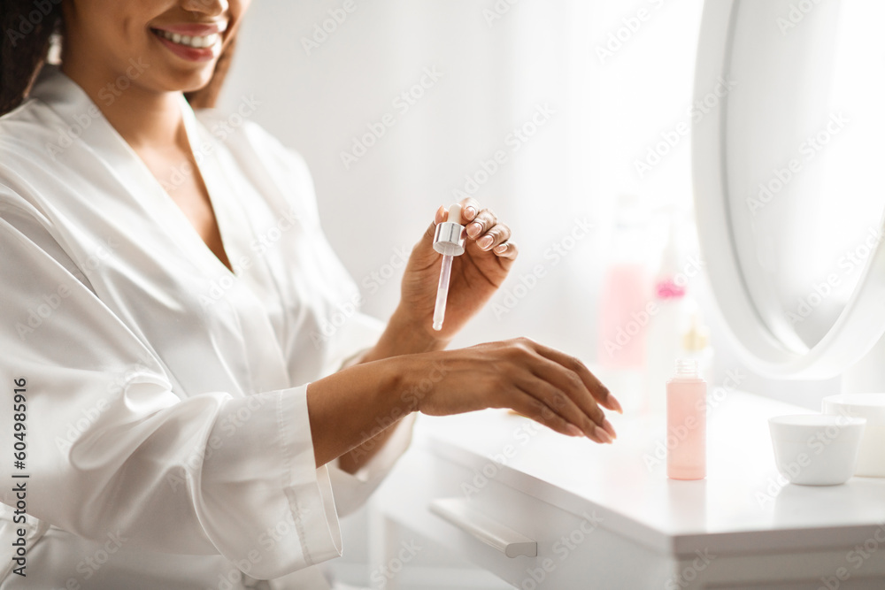 Smiling african american woman applying serum on her hand at home Smiling african american woman applying serum on her hand at home