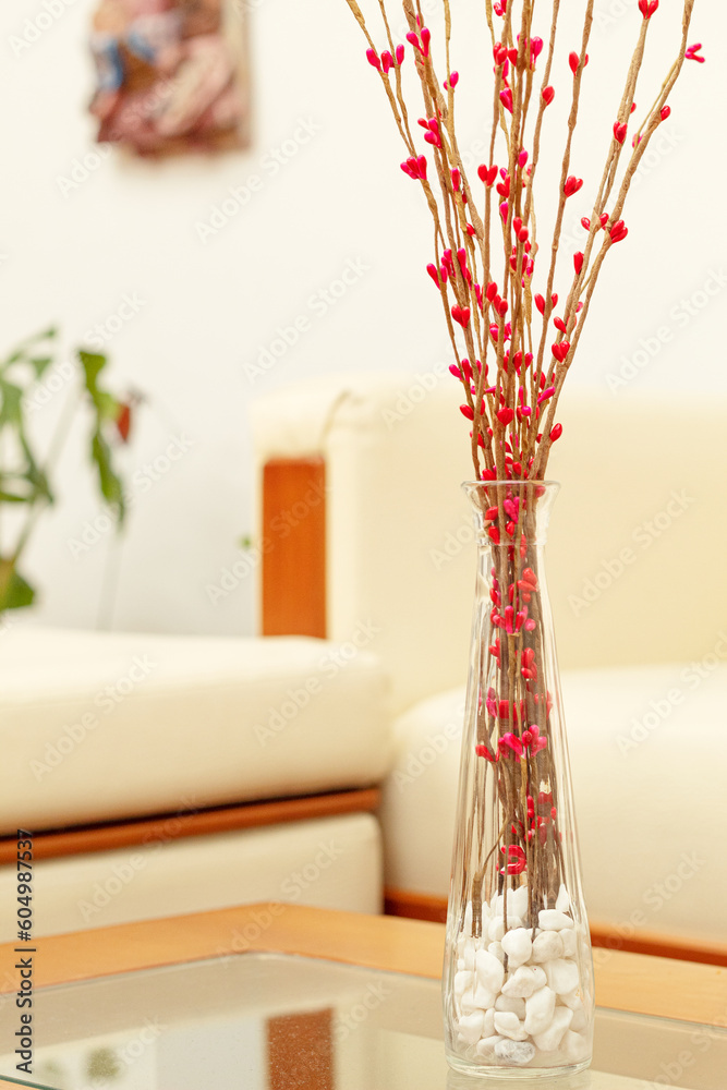 A vase with decorative artificial flowers in a living room with a defocused background