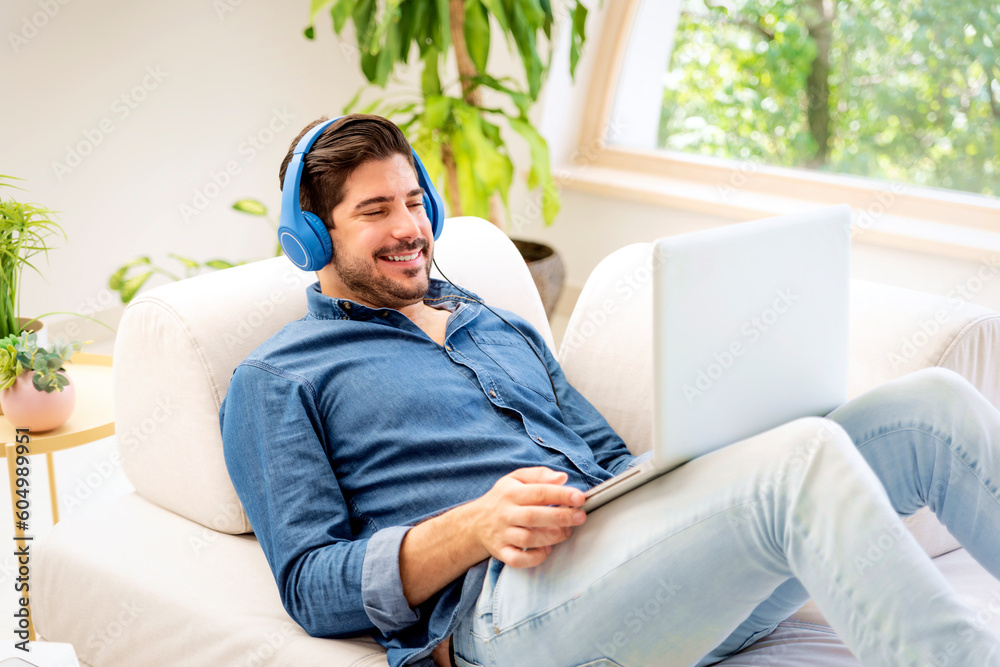 Confident man wearing headphone and using laptop while relaxing at home