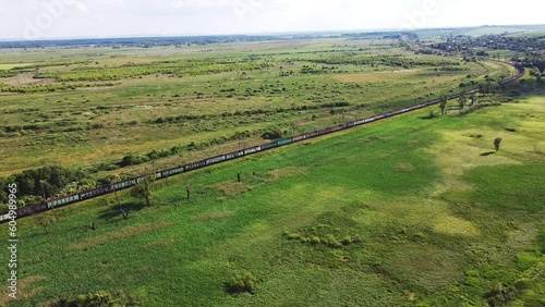 Freight-long trains carry with carriages a locomotive by the arid hilly landscape. Aerial drone perspective view at summer sunset. photo