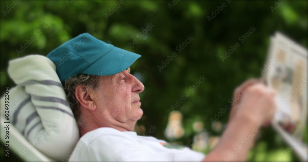 Senior man reading newspaper outdoors. Candid casual older retired person reading news
