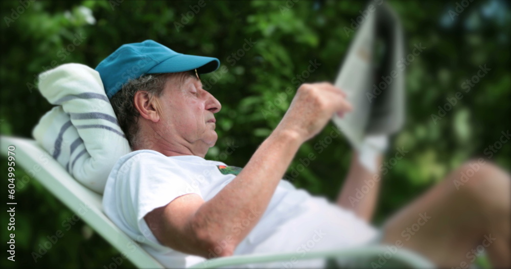 Older man reading newspaper relaxing outdoors, laid down in backyard Older man reading newspaper relaxing outdoors, laid down in backyard