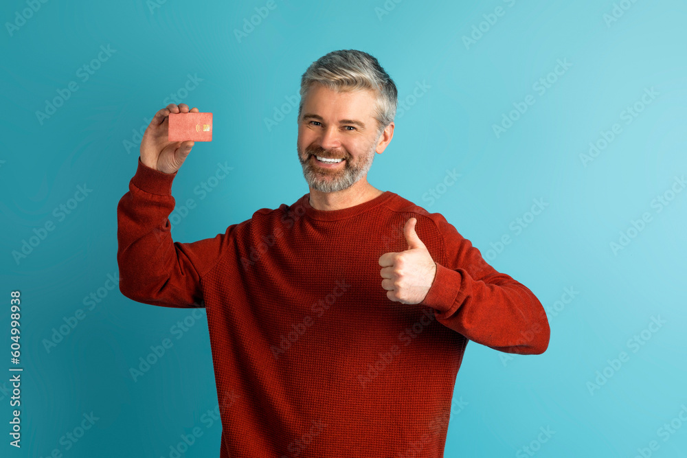 Fototapeta premium Cheerful mature man showing bank card and thumb up