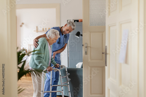 Fotografie Caregiver helping senior woman to walk in her home with walker.