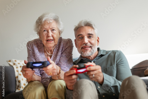 Mature man playing video games with his senior mother, having fun.
