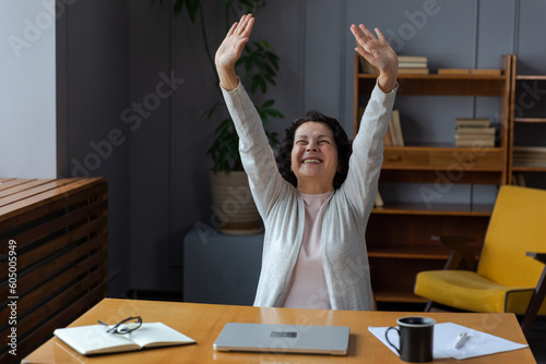 Middle aged senior woman at home relaxing stretching hands and body taking break from work on laptop. Older mature woman happy after work done satisfied by good result. Fatigue from long laptop usage