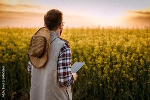 Back view of a Caucasian farmer standing in front of the field at sunset.