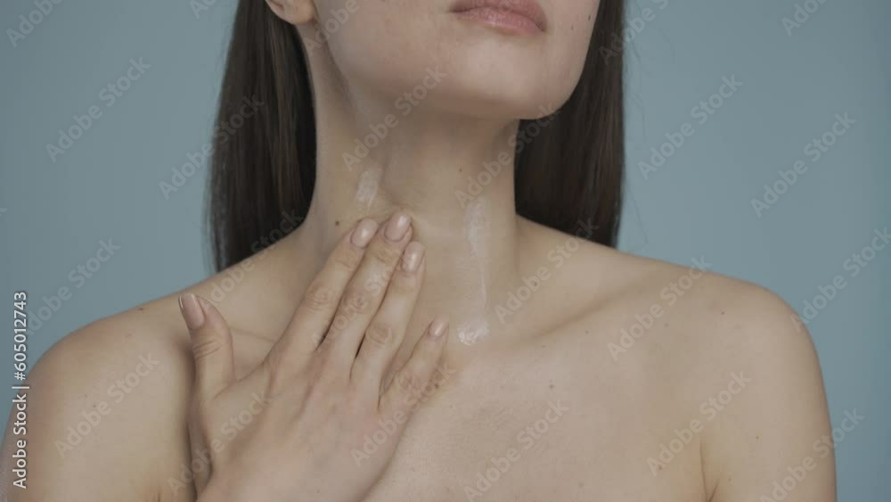 A woman applies cream to her neck and upper body. With slow massage movements, a woman rubs the cream into the skin close-up on a blue background. Natural beauty. HDR BT2020 HLG Material. A woman applies cream to her neck and upper body. With slow massage movements, a woman rubs the cream into the skin close-up on a blue background. Natural beauty. HDR BT2020 HLG Material.
