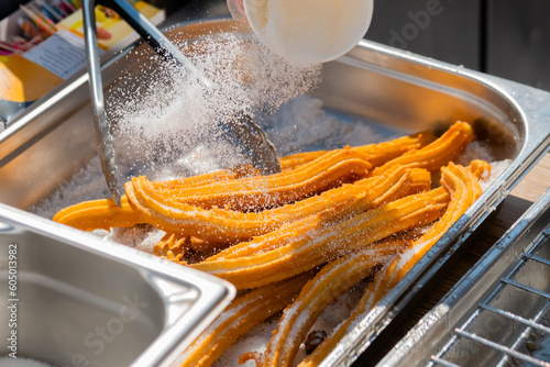 Chef preparing homemade crunchy churros with powdered sugar at summer outdoor food market - close up view. Traditional spanich cuisine, cookery, gastronomy and street food concept