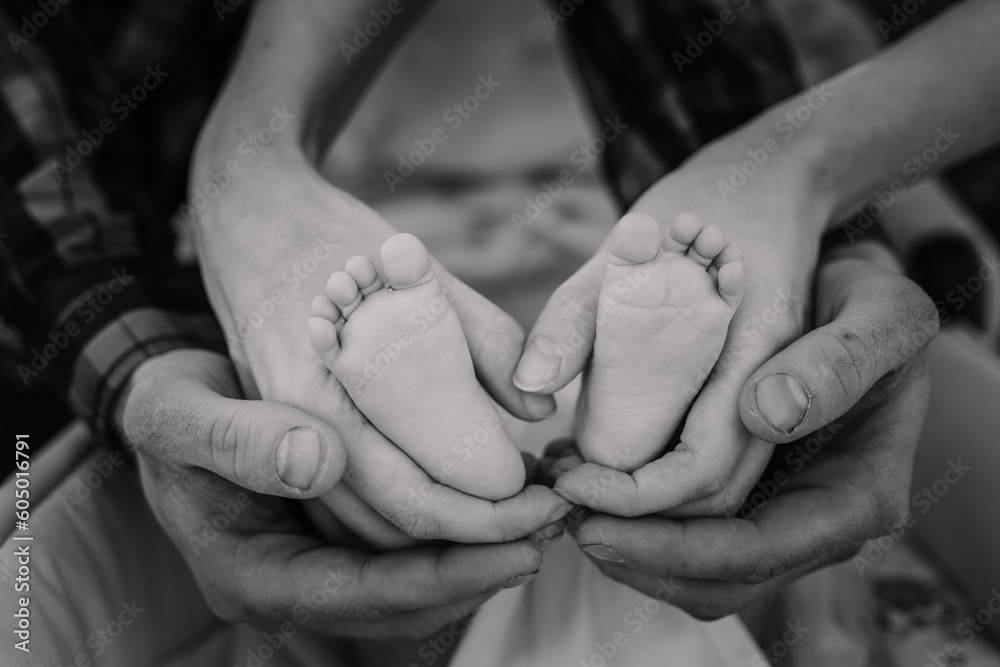 Children's leg in the hands of mother, father, parents. Feet of a tiny newborn close up. Little baby foot. Mom and her child. Happy family concept. Black and white photo of motherhood. Children's leg in the hands of mother, father, parents. Feet of a tiny newborn close up. Little baby foot. Mom and her child. Happy family concept. Black and white photo of motherhood.